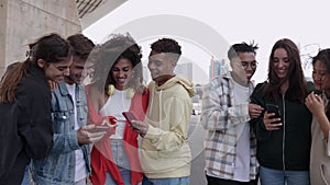 Young group of happy people laughing while using mobile phone together outdoors