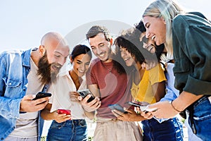 Young group of happy people smiling while using mobile phone together outdoors