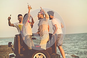 Young group having fun on the beach and dancing in a convertible car