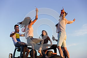 Young group having fun on the beach and dancing in a convertible car