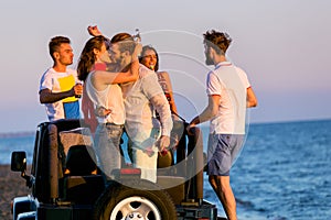 Young group having fun on the beach and dancing in a convertible car