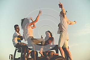 Young group having fun on the beach and dancing in a convertible car