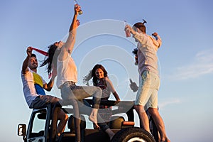 Young group having fun on the beach and dancing in a convertible car