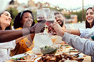 Young group of people enjoying dinner reunion in the evening at rooftop home.