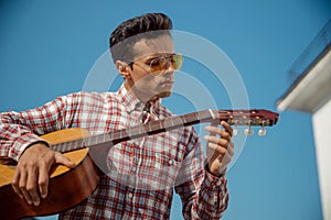 Young guitar player tuning his instrument outdoors