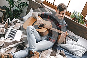 Young guitarist hipster at home with guitar in bedroom playing happy