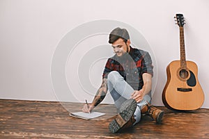 Young guitarist hipster at home with guitar sitting writing song