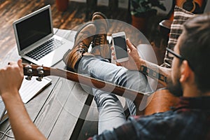 Young guitarist hipster at home with guitar tuning using app close-up