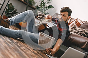 Young guitarist hipster at home sitting on the floor with guitar reading notes