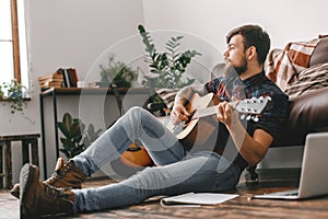 Young guitarist hipster at home sitting on the floor playing guitar dreaming
