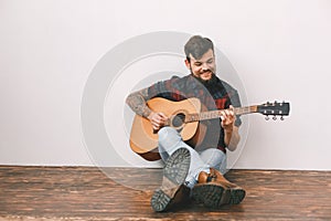 Young guitarist hipster at home sitting on the floor playing guitar smiling