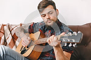 Young guitarist hipster at home sitting playing guitar serious