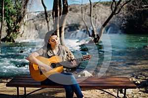 Young guitarist playing acoustic guitar and looking to river nature.Searching inspiration.Music creator.New artist in good mood.