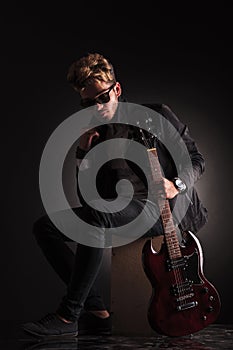 Young guitarist sitting and holding his jacket by it's collar