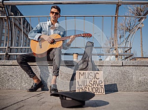 Young guitarist sitting and playing on the street