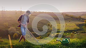 A young guy 17 years old plant a tree. Digging a hole with a shovel, next to an apple tree seedling. Against the