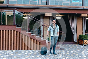 Young Guy Arab Businessman Student Came go to Restaurant With Suitcase in Hand, Smiling at Camera, Stops and Looks Away.