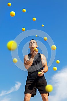 Young guy athlete juggles yellow balls outdoors. Sports concept. photo