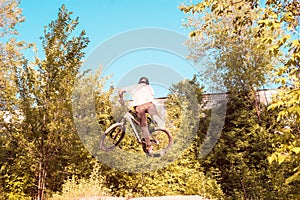 a young guy, an athlete, performs tricks with a bike, jumps on the springboard. in the forest. against the setting sun