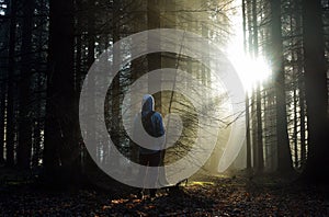 Young guy with a backpack standing in a forest in the mist at sunrise