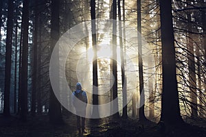 Young guy with a backpack standing in a forest in the mist at sunrise