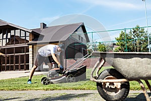 Young guy in the backyard unscrews the fuel tank cap of a lawn mower.