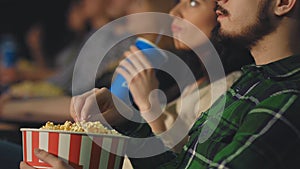 A young guy with a beard eats popcorn in the cinema