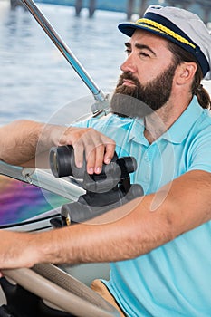A young guy with a beard sails on a yacht at the helm with binoc