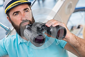 A young guy with a beard sails on a yacht at the helm with binoc photo
