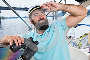 A young guy with a beard sails on a yacht at the helm with binoc photo