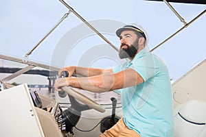 A young guy with a beard swims on the yacht at the helm