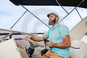 A young guy with a beard swims on the yacht at the helm