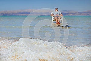 The young guy brunet sunbathes on a chair in the dead sea. View of the Jordan Mountains from the shores of the Dead Sea in Israel.