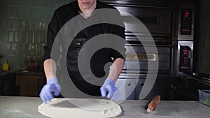 Young guy in chef uniform twirls and throws pizza dough in the restaurant kitchen.