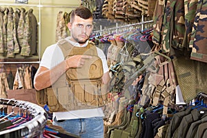 Young guy choosing flak jacket in military shop