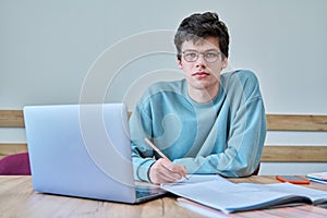 Young guy college student sitting at desk in classroom, using laptop, looking at camera