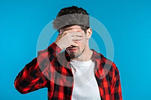 Young guy covers his face with hands from fatal disappointment, failure.