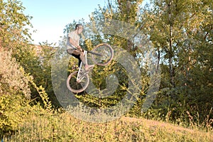 Young guy cyclist jumping high and doing tricks with a bicycle. unusual angle. in the forest against sunset