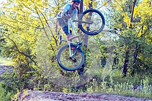 A young guy, a cyclist with tattoos, jumps on a bicycle. In the forest against the setting sun