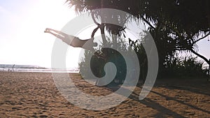 Young guy demonstrates human flag at sea beach. Athletic man doing gymnastics elements on palm tree at exotic ocean