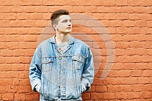 Young guy in a denim jacket against a brick wall. copyspace