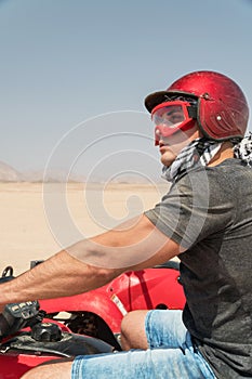 Young guy during desert excursion by quad - Man in helmet and adventure clothes in exotic scenarios - Concept of activity holiday,