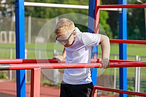 a young guy does push-ups on bars on a sports ground in the summer