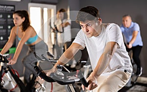 Young guy doing cardio workout on exercise bike in gym