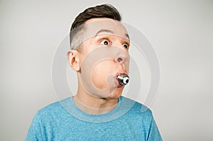 Young guy dressed in a blue t shirt hold in hand and eat light bulb lamp on a light background