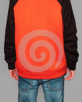 A young guy dressed in a orange and black hoodie standing backwards