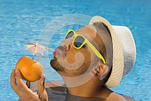 Young guy drinking fresh grapefruit juice in the swimming pool