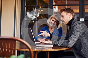 Young guy in formal clothes have a business talk with old woman in cafe