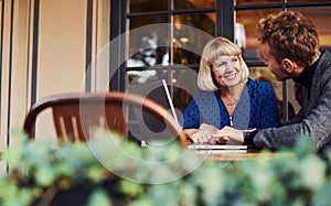 Young guy in formal clothes have a business talk with old woman in cafe