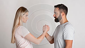 Young guy and girl look at each other seriously and squeeze their hands in arm wrestling